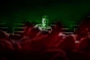 Na spowitej zielonkawą mgłą widowni teatralnej siedzi zamyślony reżyser spektaklu. Na pierwszym planie kłębowisko niewyraźnych postaci. 